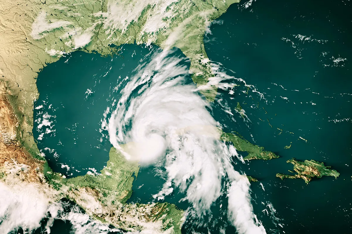 A high-angle satellite view of a large hurricane with a defined eye-wall moving through the Gulf of Mexico toward the United States coastline, situated between the Yucatán Peninsula, Cuba, and Florida