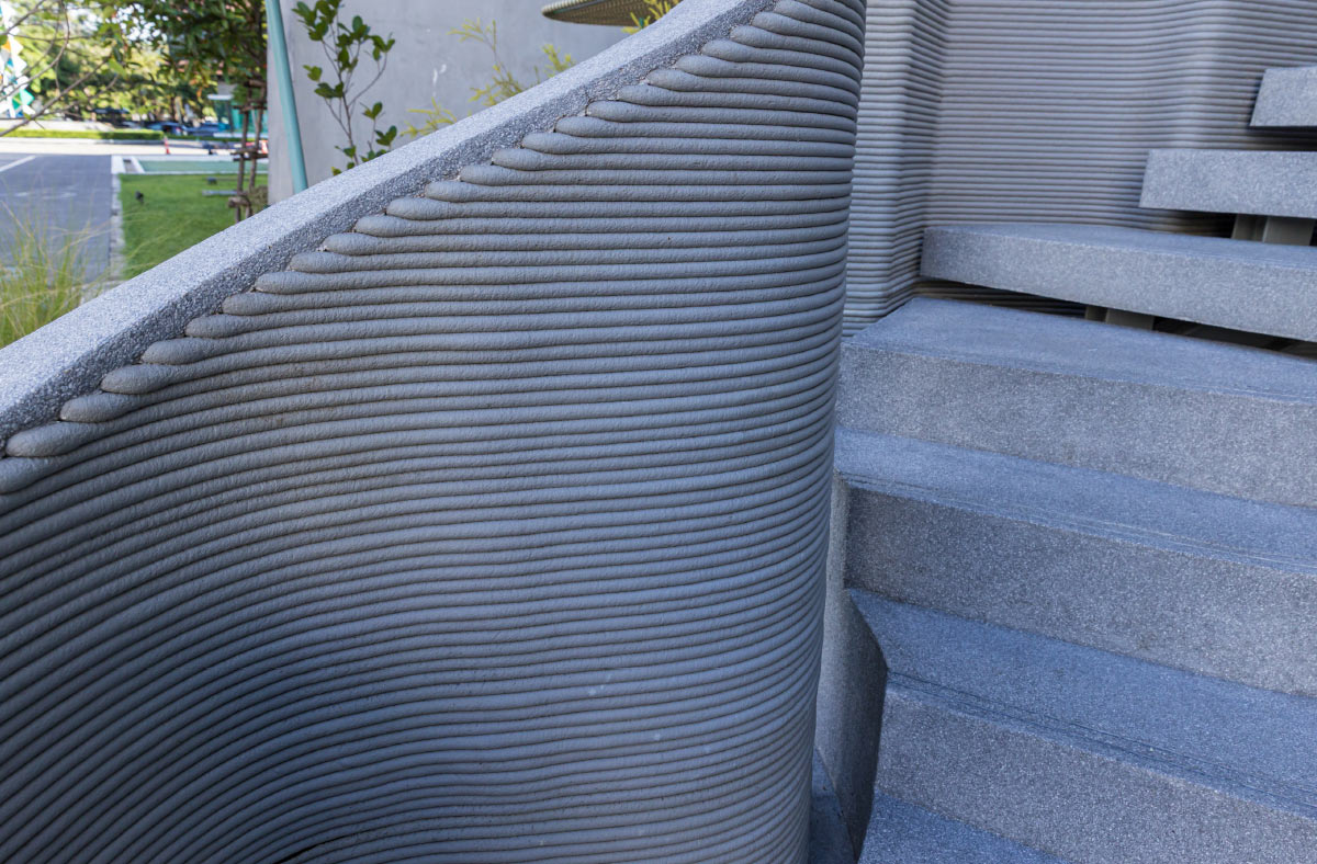 Close-up of layered 3D-printed concrete walls showing the distinctive horizontal texture alongside finished smooth concrete steps.