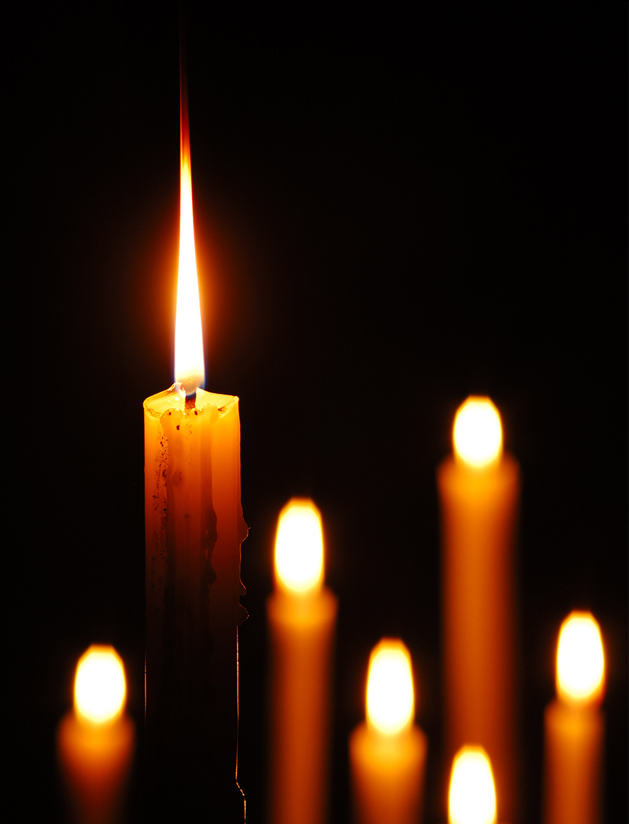 A group of lit taper candles against a deep black background.